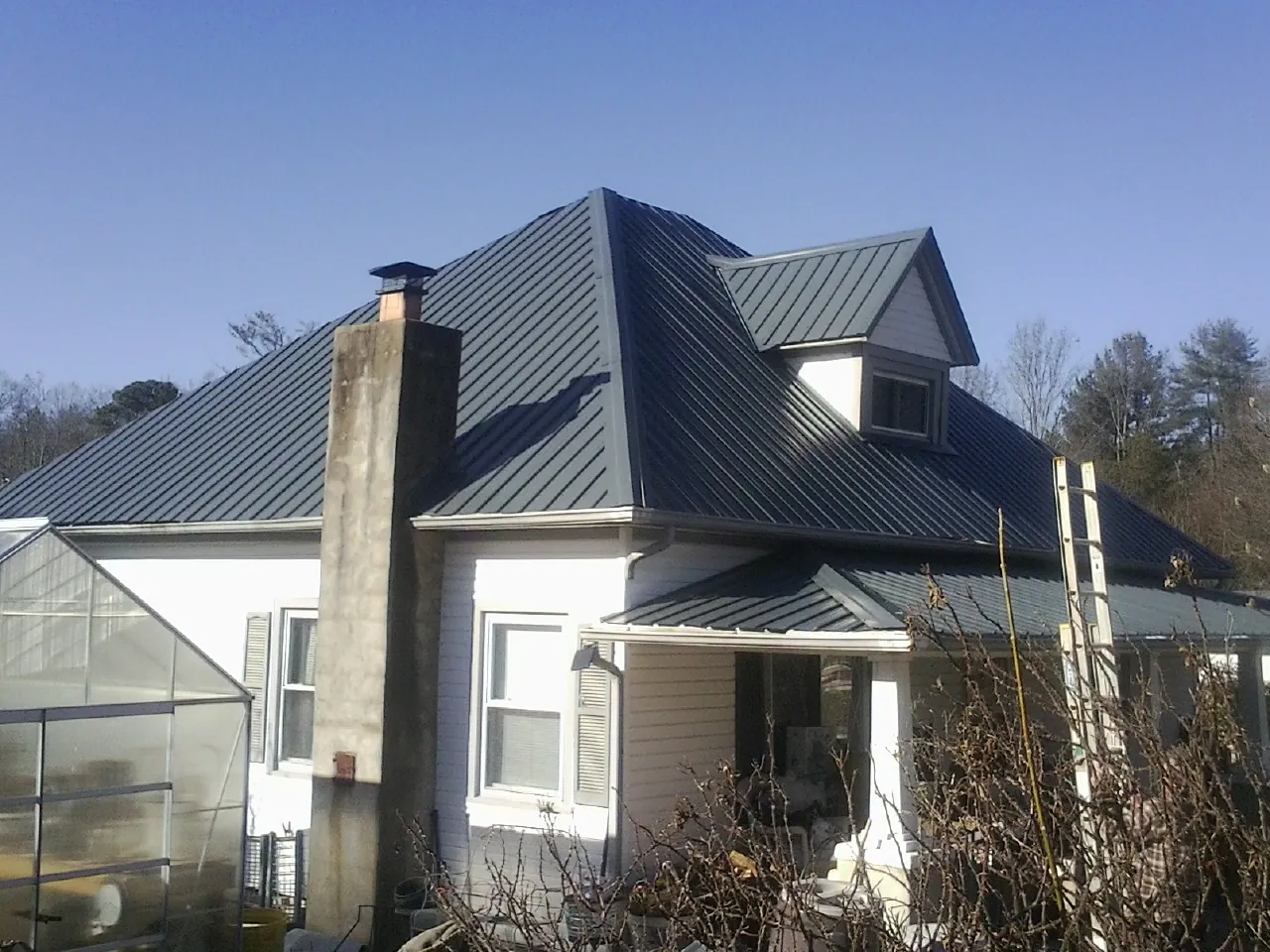 Dark blue standing seam metal roof on a white farmhouse with dormer in Port Chester