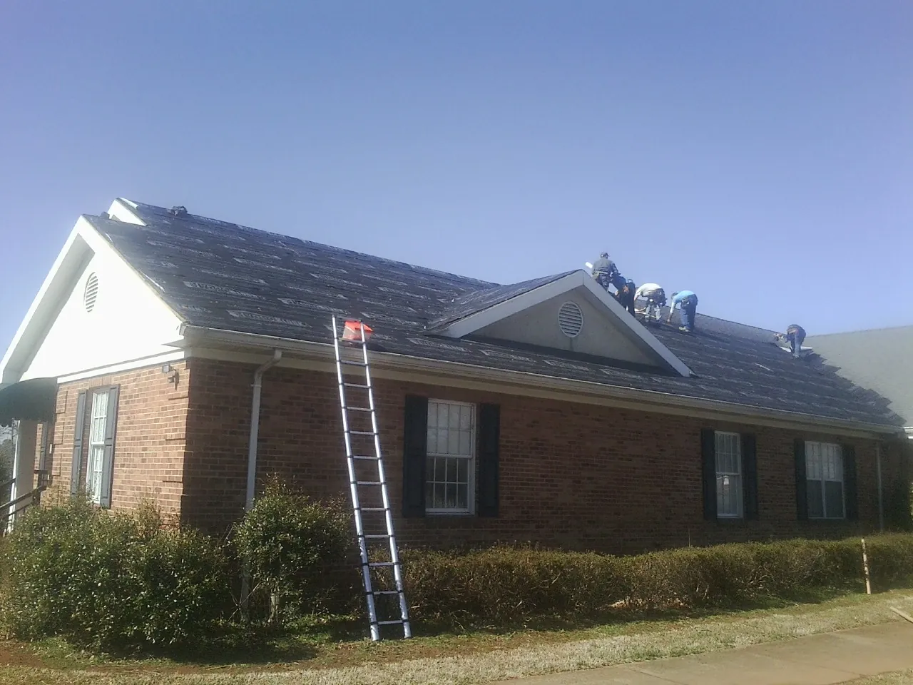 Crew tearing shingles off a brick ranch roof with a ladder set — Metal Roof Repair work by our crew in Port Chester