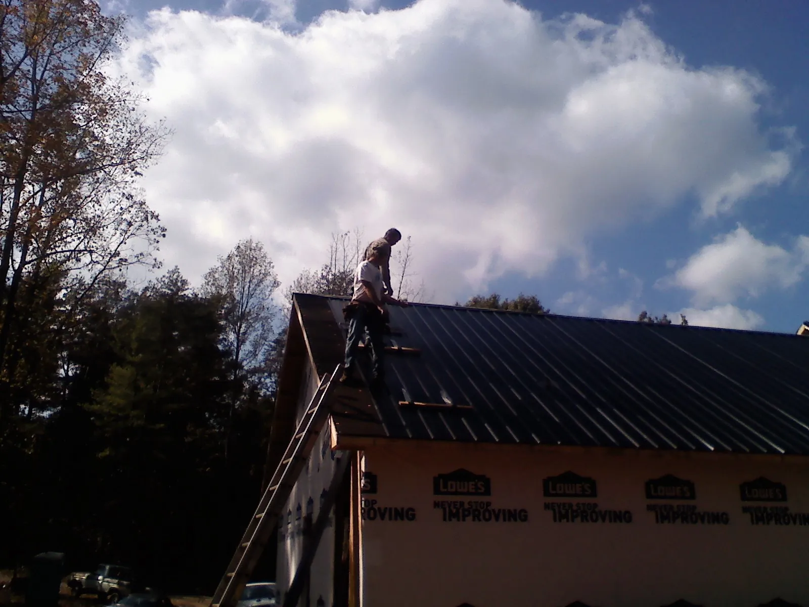 Roofer fastening dark metal panels high against a cloudy sky, from a Roof Inspection job in Port Chester