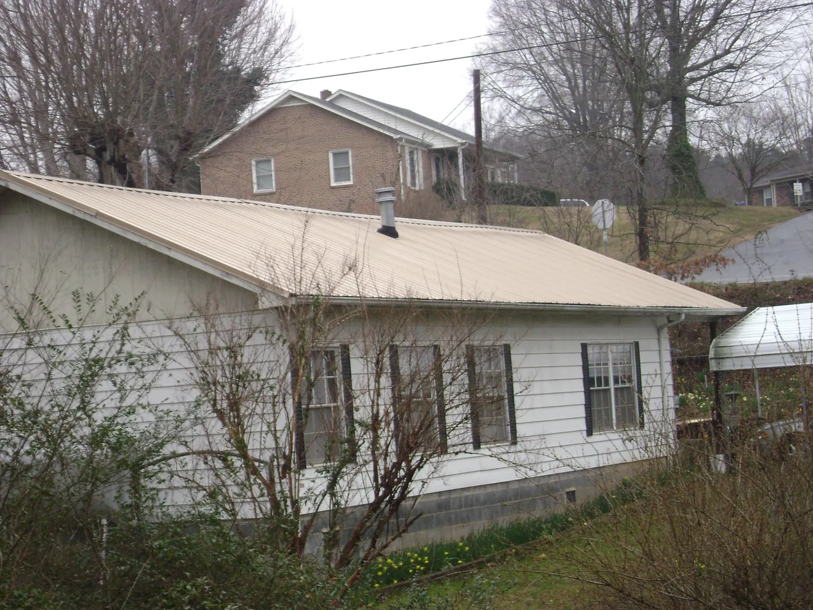 Tan metal roof on a white sided house set into a hillside — Commercial Roofing by Roofing Brothers in Port Chester